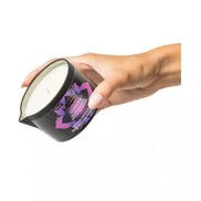 Kama Sutra Island Passion Berry massage candle in a black container, held by a hand, with a white wax top.