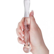 Clear glass massager held in a hand, featuring a smooth, elongated design with rounded ends.