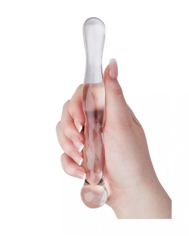 Clear glass massager held in a hand, featuring a smooth, elongated design with rounded ends.
