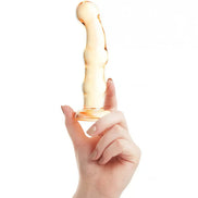 Lucent Soleil glass massager held in a hand, featuring a smooth, curved design in a translucent amber color.
