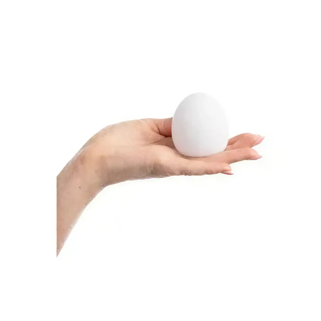 White masturbator egg held in a hand, showcasing its smooth surface and rounded shape.