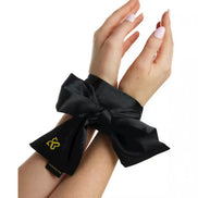 Black satin bondage ties with a large bow, secured around wrists, featuring a gold logo tag.