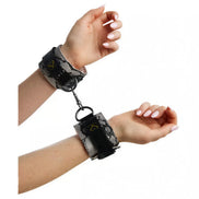 Luxury handcuffs with a snake print design, secured around wrists, featuring a metal chain connector.