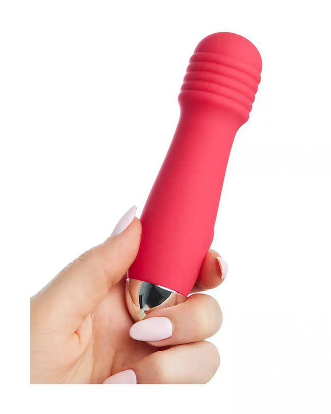 Mini wand vibrator in bright pink silicone with a metallic tip, held in a hand with manicured nails.