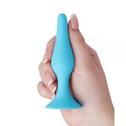 Medium silicone butt plug in blue held by a hand, featuring a tapered tip and flared base for safety.
