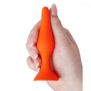 Medium silicone butt plug in bright orange, held in a hand, featuring a tapered tip and flared base for safety.
