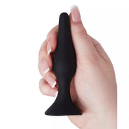 Medium silicone butt plug held in a hand, featuring a smooth black surface and tapered design for easy insertion.
