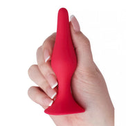 Medium silicone butt plug in red, held in a hand, featuring a tapered tip and flared base for safety.