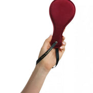 Luxury paddle in red with a black wrist strap, held in a hand against a white background.