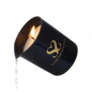 Black massage candle with a gold logo, lit wick, and melted wax dripping from the side.