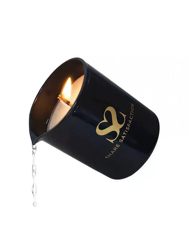 Black massage candle with a gold logo, lit wick, and melted wax dripping from the side.