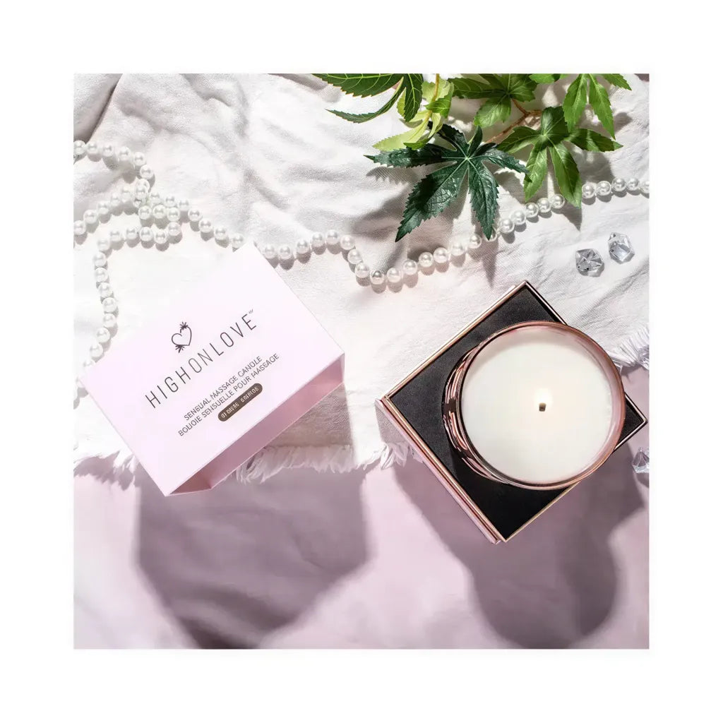 High On Love massage candle in a black and gold container, placed on a soft fabric with greenery and decorative pearls.