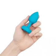 B-Vibe vibrating jewel plug in bright blue held in a hand, showcasing its tapered design and smooth surface.