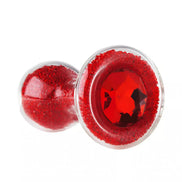 Lucent glass butt plug in red with a gem-like design and a transparent body, showcasing decorative red glitter.
