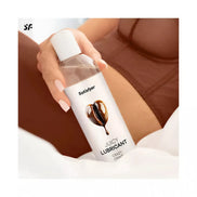 Satisfyer Juicy Lubricant, 300ml bottle with a heart design, placed on a soft surface next to a person in lingerie.