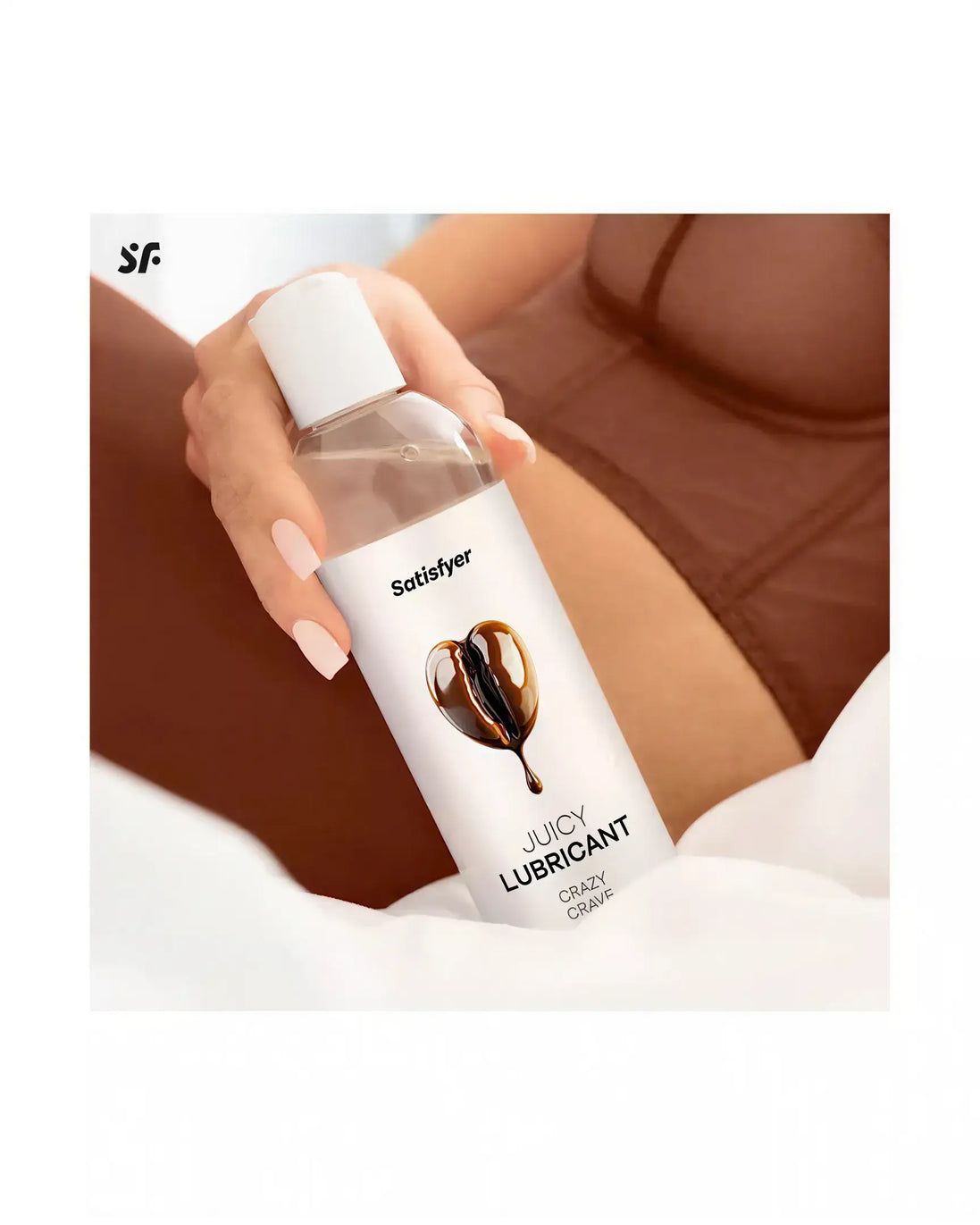 Satisfyer Juicy Lubricant, 300ml bottle with a heart design, placed on a soft surface next to a person in lingerie.