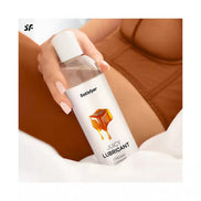 Satisfyer Juicy Lubricant, 300ml bottle with creamy caramel design, held by a person in brown lingerie on a white surface.
