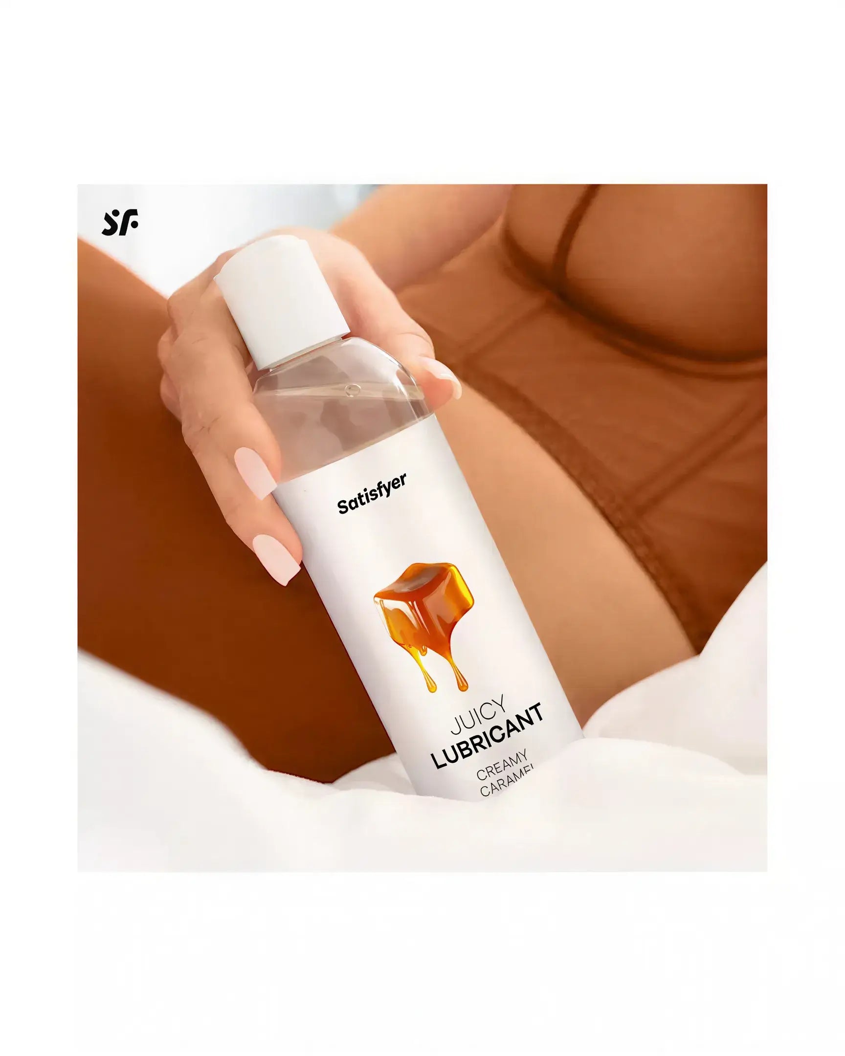 Satisfyer Juicy Lubricant, 300ml bottle with creamy caramel design, held by a person in brown lingerie on a white surface.