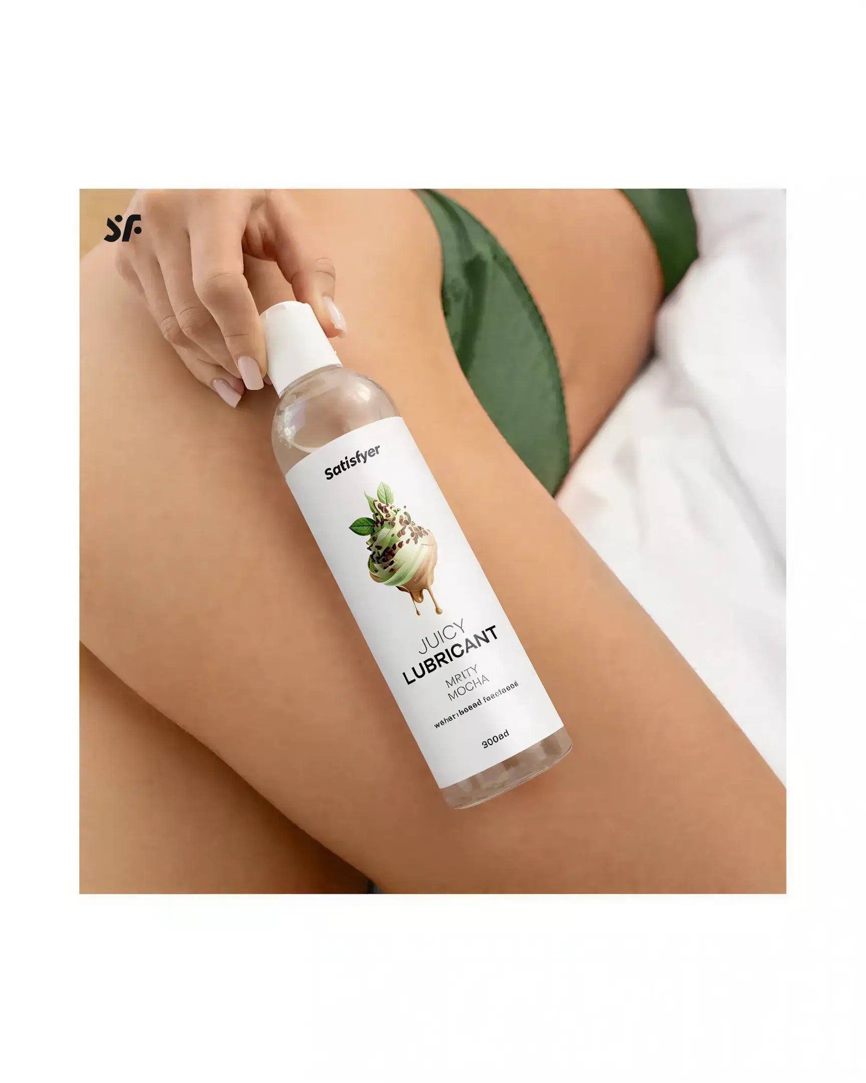 Satisfyer Juicy Lubricant 300ml bottle with minty mocha flavor, held by a hand on a thigh with green fabric.