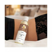 Satisfyer massage oil vanilla 250ml bottle placed on a bed with lace fabric in the background.