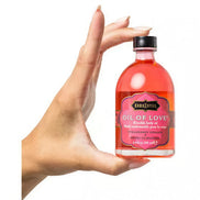 Kama Sutra Treasure Trove Oil of Love in a pink bottle held by a hand, featuring a black and gold label.