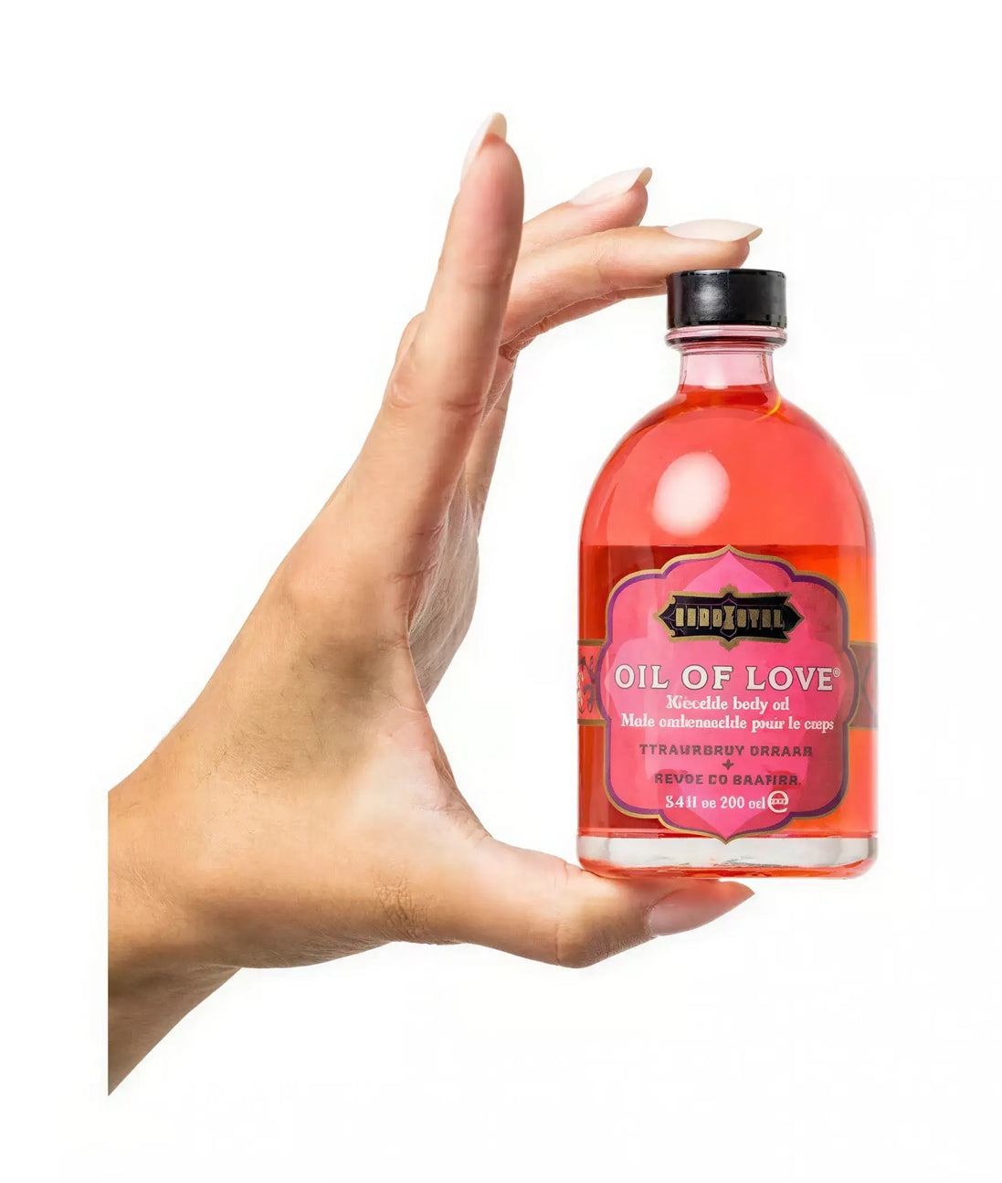 Kama Sutra Treasure Trove Oil of Love in a pink bottle held by a hand, featuring a black and gold label.